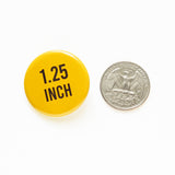 a round yellow 1.25" pinback button next to a quarter for size.