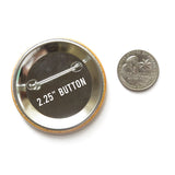 Back of a 2.25" metal pinback button next to a Quarter coin for size comparison.