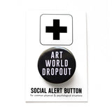 Round black pinback button that reads ART WORLD DROPOUT in white text. Button is on a Social Alert Button backing card. 
