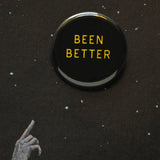 A round black pinback buton that reads BEEN BETTER in yellow text.