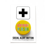 Round yellow pinback button that reads BIRTHDAY PERSON in alteranting pink & purple text, and blue and green text. with the I as a little candle. The button is pinned to a Social Alert Button backing card.