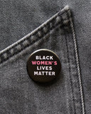 Round black pinback button that reads BLACK WOMEN'S LIVES MATTER, in white with Women's in pink for emphasis. Button is pinned to black denim.