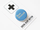 Round, light blue pinback button with cream text that reads BON VIVANT on two lines. Pinned to a Social Alert Button backing card.