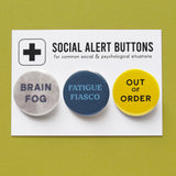 3 round multi-colored pinback buttons lined up on a SOCIAL ALERT BUTTONS backing card. Reading left to right: Brain Fog, Fatigue Fiasco, Out of Order