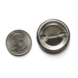 Back of a metal pinback button next to a quarter for size comparison.