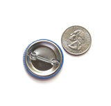 Back of a metal pinback button next to a quarter for size comparison.