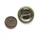 back of a metal pinback button next to a quarter for size comparison