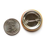 Back of a round metal pinback button next to a quarter for size reference
