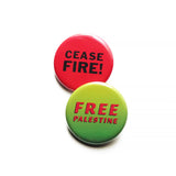 Two overlapping pinback buttons. The round button in the forefront is a neon green ombre that reads FREE PALESTINE in red text. The one behind is a round red pinback button that reads CEASE FIRE ! in black text. 
