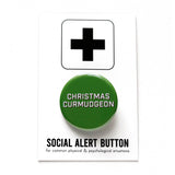 Round, dark green pinback button that says CHRISTMAS CURMUDGEON in white text with a black shadow. Button is on a Social Alert Button backing card.