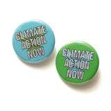 Two round pinback buttons that read CLIMATE ACTION NOW, the left one is ice blue, the right one is bright green.