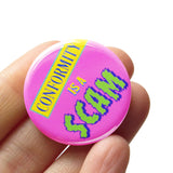 Round bubblegum pink 1.25" pinback button that reads CONFORMITY IS A SCAM in colorful mixed fonts that have a retro 80's vibe. Button is held in a hand.