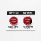 A button set on perforated edge card on minty green background. Left pin reads COOKIE BAKER in mint green in shape of holiday cookie. Right pin reads COOKIE EATER in mint green, with a bite missing and cookie crumbs.