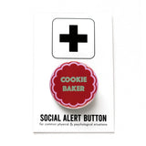Round pink pinback button with a cookie shape that reads COOKIE BAKER in mint green text. Pinback button is on Social Alert Button Backing Card.