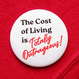 A round white  pinback button that reads THE COST OF LIVING IS TOTALLY OUTRAGEOUS in black & red text,  in two fonts, with a retro 80's vibe.  Button is on a red sweatshirt.
