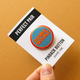 Two pinback buttons in inverse blue, orange and yellow colors that reads DOUBLE TROUBLE, each on a Perfect Pair backing card that perforates and tears down the middle to split the buttons, Keep One, Share One.