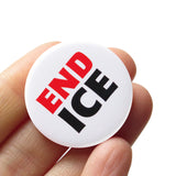 a round white pinback button that reads END ICE in a chunky Red & Black font. Button is held in a hand.