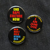 Three round 1.25" black button with neon orange, yellow & blue text that read END RAPE CULTURE NOW, I AM JANE DOE, and MEN MUST HOLD OTHER MEN ACCOUNTABLE pinned to black denim.