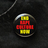 Round black pinback button that reads END RAPE CULTURE NOW in neon yellow and orange san serif text. The button is pinned to black denim jeans.