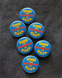 Six round blue pinback buttons that reads END THE GEN0CIDE IN GAZA in yellow & orange bold text. Buttons are pinned to black denim.