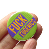 a round 1.25" pinback button with a lime green grid pattern background that reads  FUCK EUGENICS in golden yellow text with purple rectangles behind. Button is held in a hand.
