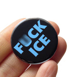 a round black button that says FUCK ICE in a chunky light blue font. Badge is held in a hand. U is blurred in photo.