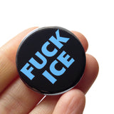 a round black button that says FUCK ICE in a chunky light blue font. Badge is held in a hand.