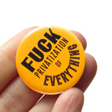 a round orange yellow 1.25" pinback button that reads FUCK Privatization Of Everything in black text. Button is held in a hand.