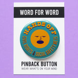 A round teal pinback button that reads HANDS OFF Civil Rights & Social Safety Nets yellow-orange text,  with an angry shouting face in the center of the button. Button is on a Word For Word branded backing card that reads Pinback Button, Wear What's On Your Mind