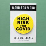 Big round neon yellow pinback button reads HIGH RISK FOR COVID in bold black text. On a white backing card, WORD FOR WORD  brand across the top. Bold StatementS, Loud & Clear at the bottom of the card.