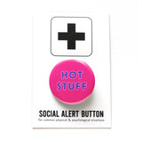 A round bright pink pinback button that reads HOT STUFF in two lines in purple text. Button is on a white backing card that reads SOCIAL ALERT BUTTON in black text with a plus sign at the top.