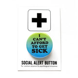 A round 1.25" pinback button with a green to blue ombre that reads I CANT AFFORD TO GET SICK in thick black text. On a branded white backing card, black plus sign at the top. Below reads: Social Alert Button, with tiny text beneath it which says, for common physical & psychological situations