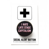 Round black pinback button that reads I HATE LATE STAGE CAPITALISM in white text with a red drop shadow. Button is on a Social Alert Button backing card.