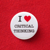 Round white pinback button that reads I LOVE CRITICAL THINKING, love being a red heart. Pinned to red sweatshirt