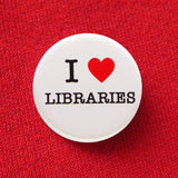 A round white pinback button that reads I LOVE LIBRARIES, love being represented by a red heart. Button is pinned to a red sweatshirt.