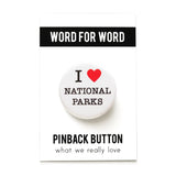 A round white pinback button that reads I LOVE NATIONAL PARKS. Love represented by a red heart. Button is pinned to a Word For Word What We Really Love branded backing card.