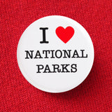 A round white pinback button that reads I LOVE NATIONAL PARKS. Love represented by a red heart. Button is pinned to a red sweatshirt