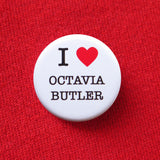 Round white pinback button that reads I Love Octavia Butler. Love is represented by a red heart, text is black. Button is on a red sweatshirt.