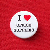 A round white pinback button that reads I LOVE OFFICE SUPPLIES, with love being indicated by a red heart. Button is pinned to a  red sweatshirt.
