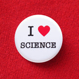 A round white pinback button that reads I LOVE SCIENCE with love being indicated by a red heart. Button is pinned to a red sweatshirt