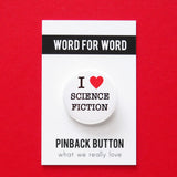 Round white pinback button that reads I LOVE SCIENCE FICTION. "Love" is represented by a red heart. Button is on a WORD FOR WORD branded card, for What We Really Love.