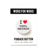 A round white pinback button that reads I LOVE VINYL RECORDS. Love represented by a red heart. button is on a Word For Word branded bakcing card
