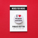 Round white pinback button that reads I LOVE WOMEN ARTISTS with a red heart indicating love. Button is on a Word For Word Pinback Button branded backing card.