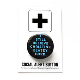 A round black pinback button that reads I STILL CHRISTINE BLASEY FORD in light blue text. Button is pinned to a Social Alert Button backing card.