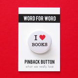 A round white pinback button that reads I LOVE BOOKS, love being represented by a red heart. Button is pinned to a Word For Word, What We Really Love branded backing card.