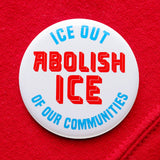 A round white 2.25" pinback button that reads ABOLISH ICE in thick red text in the center, and ICE OUT - OF OUR COMMUITIES in light blue text, above & below, curved to the round button.  Badge is pinned to a red sweatshirt.