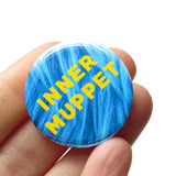 A round 1.25" pinback button with a blue synthetic puppet fur background, that reads INNER MUPPET in yellow text. Button is held in a hand.