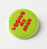 Round, lime green 1.25" pinback button off balance red text reading LOSING MY MIND. 