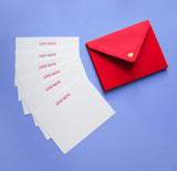 A fan of six white note cards with LOVE NOTE embossed in red gloss type at the top of each card, with a stack of red envelopes to the right, with a tiny gold heart at the close of each triangle. Notecard set is on a lavender background.