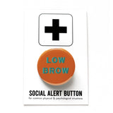 Round milk chocolate brown pinback button with aqua teal text that reads LOW BROW. Badge is on a Social Alert Button backing card.